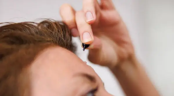 Zbliżenie na twarz kobiety, która aplikuje kroplę celimax retinal shot na czoło.