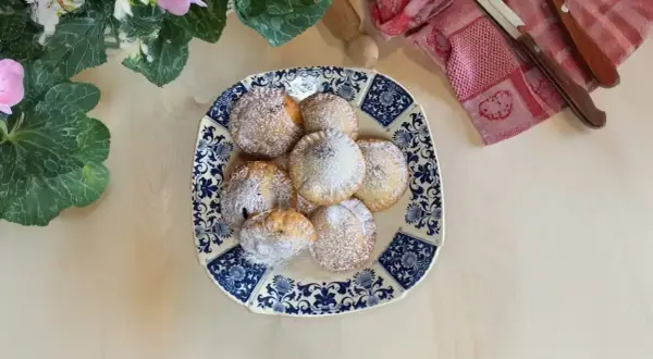 Piatto di ravioli al cioccolato spolverati di zucchero a velo, decorato con fiori e foglie verdi.