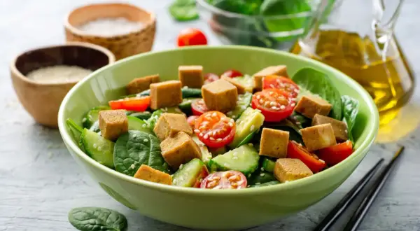 Pyszna sałatka z chrupiącym tofu, pomidorkami koktajlowymi i ogórkiem na świeżym szpinaku. Idealna na lekki posiłek.