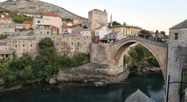 Stari Most, en ikonisk stenbro i Mostar, sträcker sig över en turkos flod. Gamla stenbyggnader och en moské omger den.