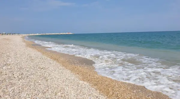Spiaggia di ciottoli a Civitanova Marche, con il mare azzurro e le onde che lambiscono la riva.