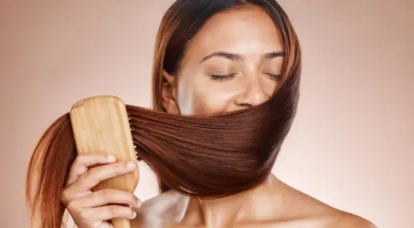 Frauen mit geschlossenen Augen bürsten ihr glänzendes, braunes Haar mit einer Holzbürste. Ein Moment der Ruhe und des **Haare pflegen**.