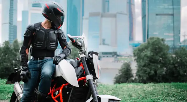 Motocyklista w zbroi ochronnej siedzi na motocyklu na tle wieżowców.