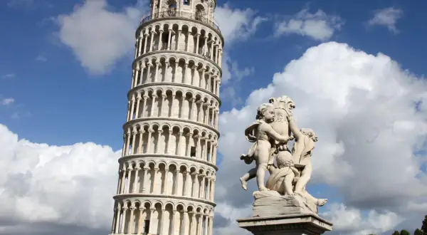 La Torre Pendente di Pisa, con la sua inconfondibile inclinazione, si erge maestosa sotto un cielo azzurro e nuvoloso, accanto a una scultura di putti.