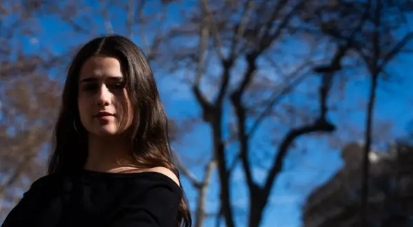 Elvira Lara, una joven con cabello castaño, mira a la cámara con un fondo de árboles y cielo azul.