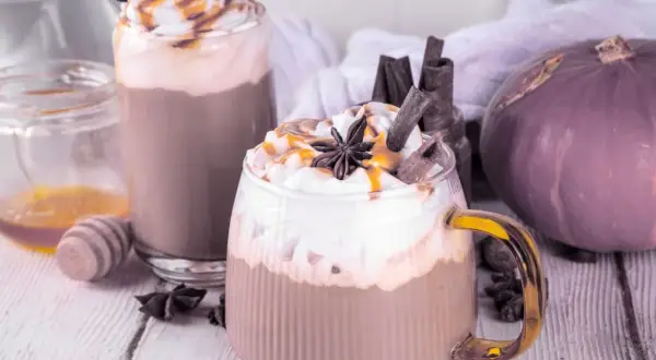 Dwie pyszne pumpkin spice latte kawa z bitą śmietaną, karmelem i cynamonem. Obok dynia i miód.