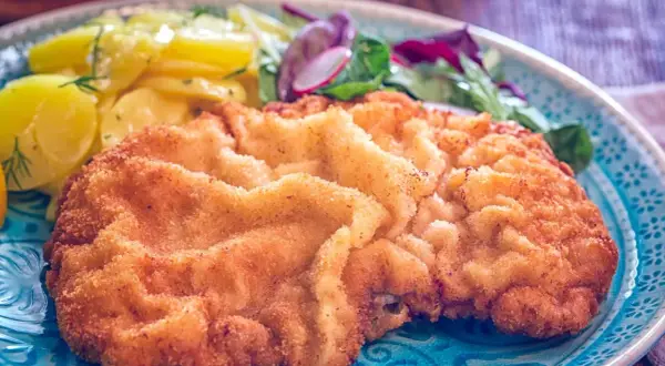 Ein knuspriges Schnitzel Wiener Art mit goldbrauner Panade, serviert mit Kartoffelsalat und frischem Grün.