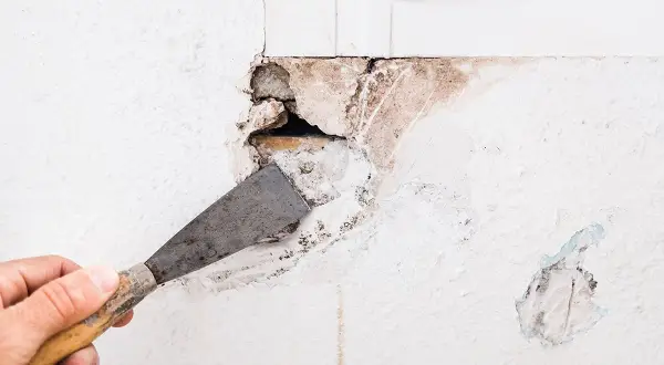 Mano con spatola che prepara un grosso buco nel muro per come riempire il muro danneggiato.