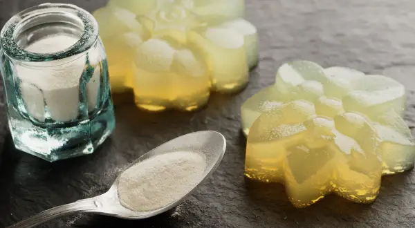 Proszek agar w słoiczku i na łyżce, obok galaretki w kształcie kwiatów. Agar to naturalny środek żelujący.