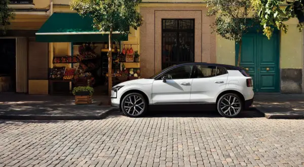 Vit Volvo parkerad på kullerstensgata framför en färggrann fasad. Upptäck olika volvo utrustningsnivåer för din nästa bil.