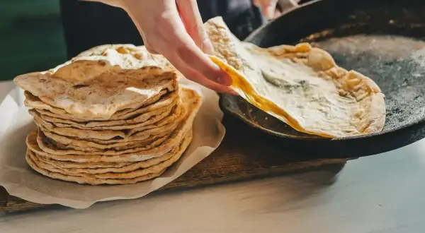 Stos świeżo upieczonego lawaszu obok patelni, na której właśnie smaży się kolejny. Pyszne, cienkie placki gotowe do podania.