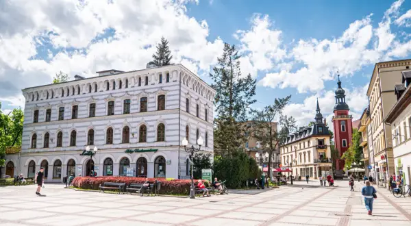 Słoneczny dzień na placu w parku zdrojowym w Cieplicach Śląskich-Zdroju. Ludzie odpoczywają na ławkach, spacerują.