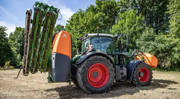 Zielony traktor z opryskiwaczem, gotowy do pracy w polu. Gdzie zrobić atest na opryskiwacz? Tutaj znajdziesz odpowiedzi.