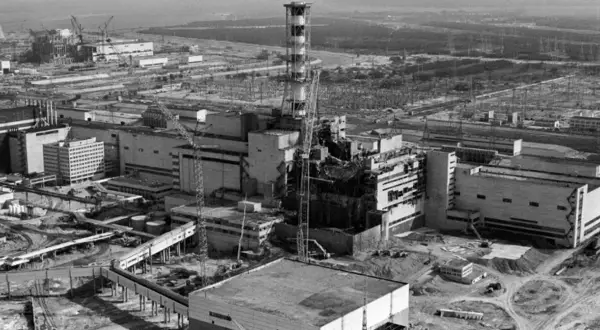 Widok zniszczonego reaktora w Czarnobylu, symbol tragedii i **czarnobyl ofiary**. W tle widać inne budynki elektrowni i żurawie.