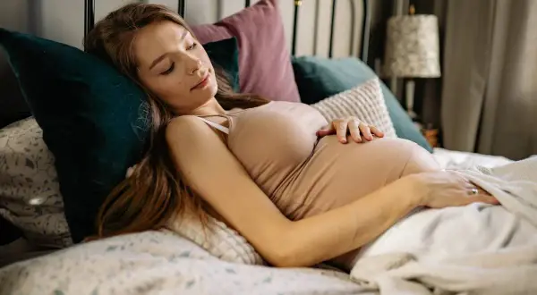 Mujer embarazada durmiendo de lado, acariciando su vientre. El embarazo boca abajo es una postura cómoda para ella.