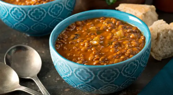 Bol de soupe de lentilles savoureuse, une recette réconfortante avec du pain et des couverts.