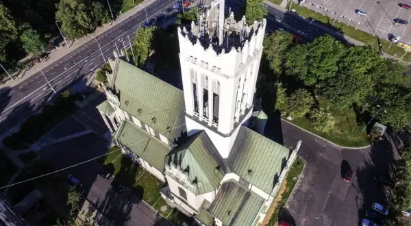 Widok z lotu ptaka na białą wieżę kościoła z zielonym dachem i otaczającą go drogę z samochodami.