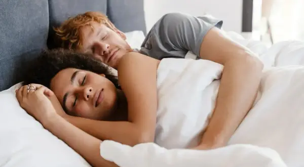 A couple sleeps peacefully, their bodies intertwined. Do you sleep better next to someone you love?