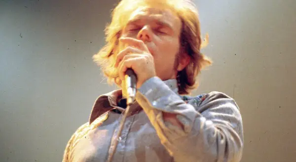 Van Morrison sings passionately into a microphone, his eyes closed. This image captures a moment from one of his legendary performances, perhaps hinting at the setlists that have defined his career.