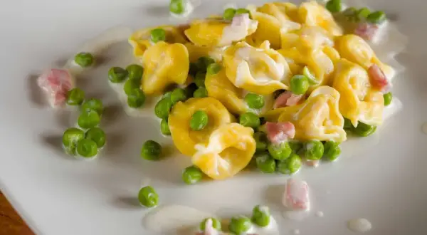 Tortellini di carne con piselli e pancetta, un classico condimento per un primo piatto gustoso e cremoso.