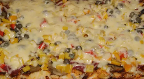 Pyszna pizza na grubym cieście z warzywami i roztopionym serem.