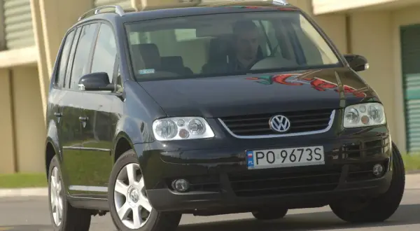Czarny VW Touran z przodu, widoczne reflektory i żarówki. Kierowca za kierownicą.
