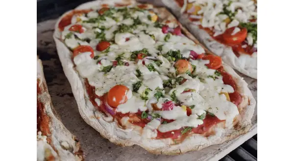 Dwie pizze na kamieniu, z pomidorkami i serem. Dowiedz się, jak przełożyć pizzę na kamień bez łopatki, by uzyskać idealnie chrupiący spód.