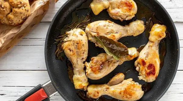 Cosce di pollo in padella, dorate e succulente, con rosmarino e alloro. Accompagnate da panini integrali.