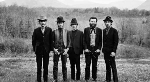 The Band, who wrote "The Weight," pose in a field with mountains in the background.