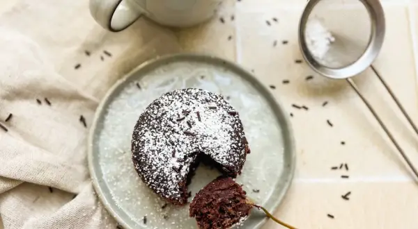 Ein saftiger Schoko-Tassenkuchen ohne Ei, bestäubt mit Puderzucker und Schokostreuseln, bereit zum Genießen.