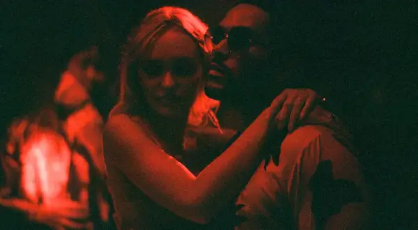 Jocelyn und Tedros in einer innigen Umarmung, beleuchtet von rotem Licht. Ein Moment aus "The Idol Serie", der die Intensität der Beziehung einfängt.