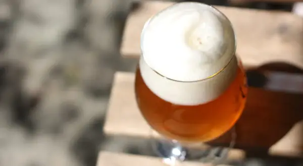 Ein Glas Bier mit viel Schaum steht auf Holzplanken. Vorsicht bei der Einnahme von Letrozol und Alkohol.