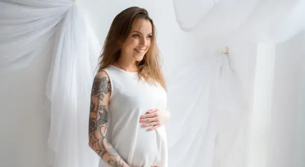 Uśmiechnięta ciężarna kobieta z tatuażem na ramieniu. Czy można zrobić tatuaż w ciąży? To pytanie nurtuje wiele przyszłych mam.