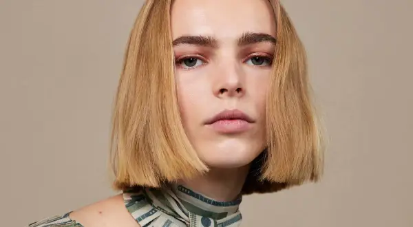 Modelka z idealnie prostymi, rudymi włosami w stylu blunt bob, z delikatnym makijażem oczu i ust, prezentuje się elegancko.