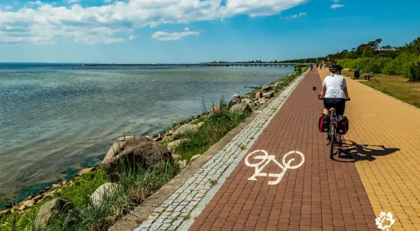 Kobieta na rowerze przemierza malowniczą trasę rowerową Władysławowo Hel. Widok na morze i molo.