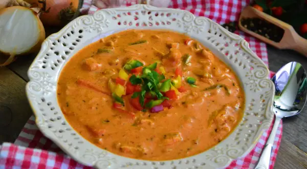 Aksamitna zupa gyros z kurczakiem i pieczarkami, udekorowana kolorową papryką i natką pietruszki. Obok leżą cebule i czosnek.
