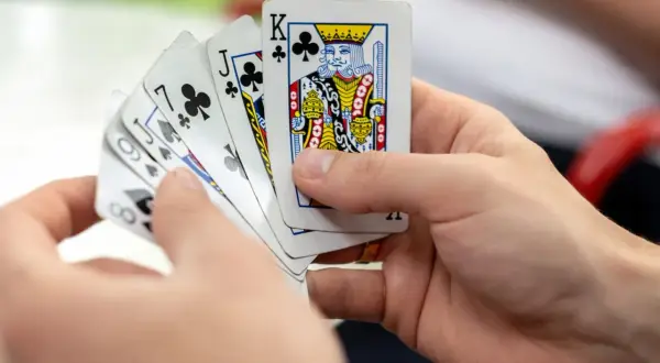 Ręce trzymają karty do gry, wśród nich król trefl. Czas na grę w kuku!