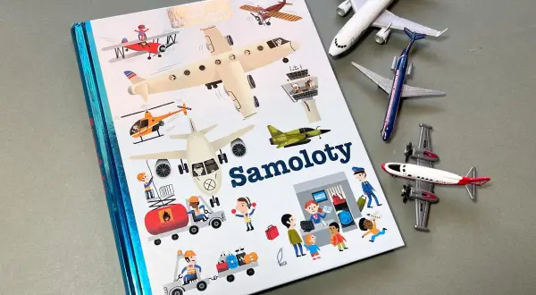 Książki o samolotach z ilustracjami różnych maszyn latających i ludzi pracujących na lotnisku. Obok leżą modele samolotów.