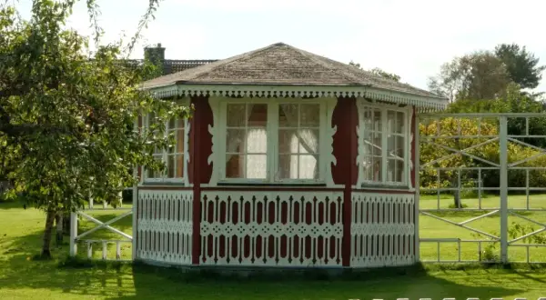 Pavillon de jardin rouge et blanc, orné de dentelle de bois. Une pomme tombe d'un arbre, peut-être pour échapper à la taxe abri de jardin.