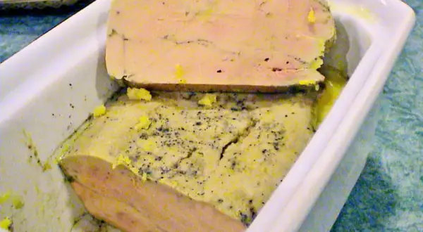 Un délice à partager : un foie gras mi cuit en terrine, parsemé de poivre, prêt à être dégusté.