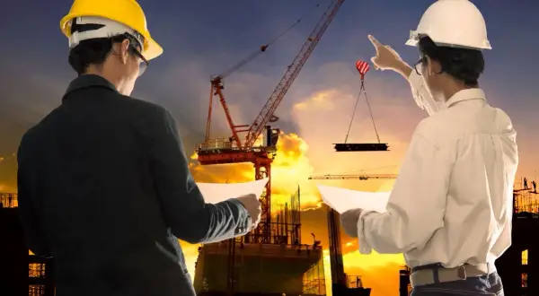 Ingegneri supervisionano un cantiere edile al tramonto, garantendo la sicurezza. Gru solleva materiale.