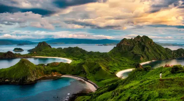 Grüne Hügel und weiße Sandstrände im Komodo Nationalpark, Indonesien. Ein einsamer Wanderer genießt die atemberaubende Aussicht auf das Meer.