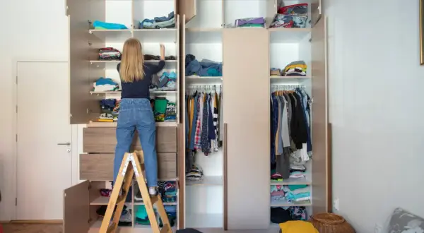 Mädchen auf Trittleiter sortiert Kleidung in einem großen Kleiderschrank, um **Stauraum schaffen**.