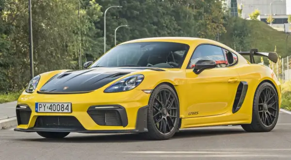 Żółty Porsche Cayman GT4 RS z czarną maską i spojlerem, gotowy do jazdy po miejskich ulicach.