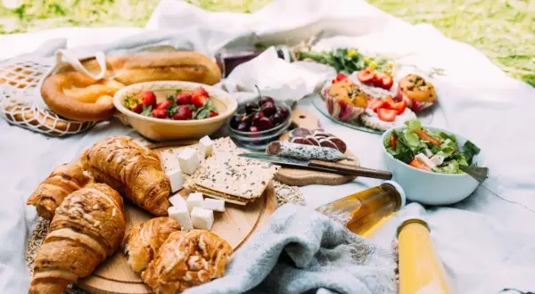 Pyszne jedzenie na piknik: świeże croissanty, bagietka, truskawki, wiśnie, sałatka, kiełbasa i napoje.