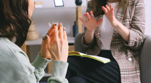 Två personer i samtal, en med gröna naglar som gestikulerar. Kanske en del av en autism utredning vuxen.