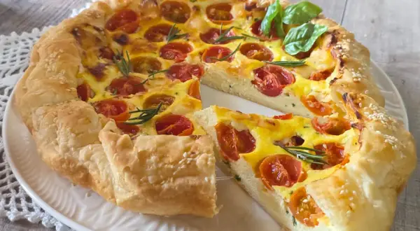 Une quiche ricotta aux tomates cerises et romarin, garnie de graines de sésame, sur une assiette blanche.
