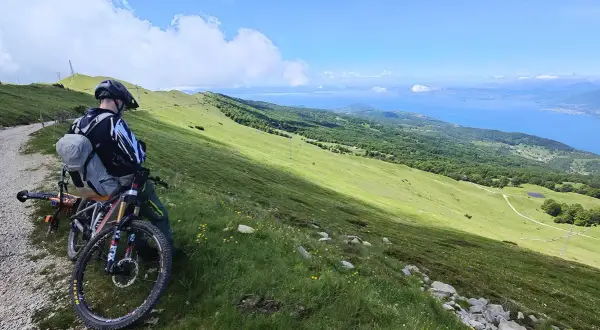 Ciclista con mountain bike ammira il panorama del lago di Garda dal Monte Baldo.