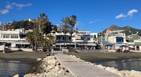 Paseo marítimo en la playa pedregalejo como llegar. Palmeras, restaurantes y montañas al fondo bajo un cielo azul.