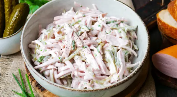 Schmackhaftes Fleischsalat-Rezept in einer Schüssel, garniert mit Schnittlauch und Gewürzgurken. Perfekt für ein schnelles Mittagessen.
